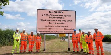 A group of people in hi-viz clothing and hard hats. In between them is a sign that reads MJ Church A 350 Chippenham Bypass Improvements Work commencing May 2025 For 18 months Working in partnership with Wiltshire Council, Department for Transport, Atkins Realis and then the web address wiltshire.gov.uk/highways-improvements