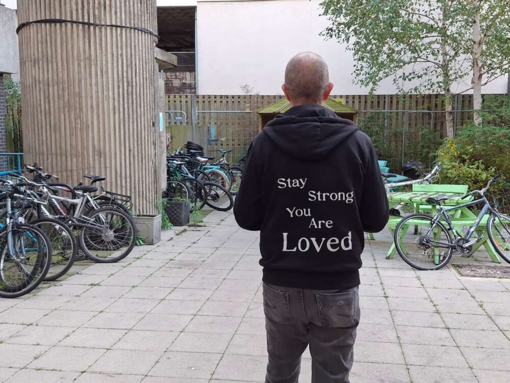 Tim Swinburn with his back to the camera. He is wearing a hoodie with the message 'You are loved'