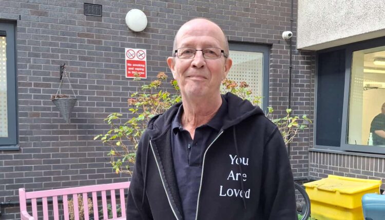 Tim Swinburn looking at the camera. He is outdoors and there is a pink bench behind him