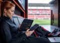 Woman holds a tablet and phone with betting interfaces in a stadium tunnel